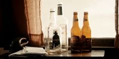 three empty bottles sitting on top of a wooden table next to a window sill