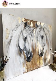 two white horses painted on a canvas in front of a desk with paintbrushes