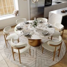 a round marble dining table surrounded by white chairs and an area rug in the kitchen