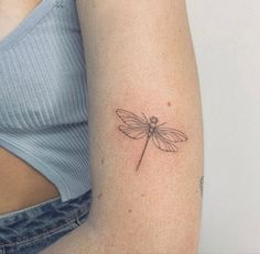 a woman's arm with a small tattoo of a dragonfly on the left shoulder