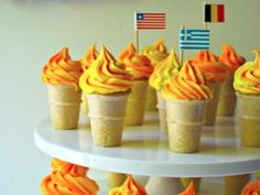 cupcakes with orange frosting and flags are on a white cake platter