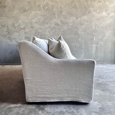 a white couch sitting on top of a cement floor next to a wall with two pillows