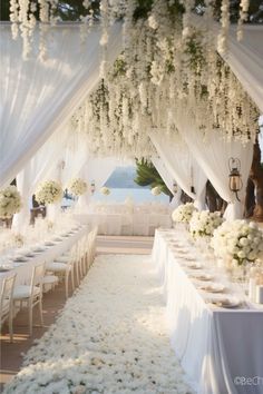 an outdoor wedding setup with white flowers and greenery on the ceiling, along with long tables