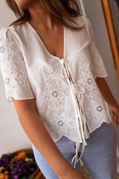 Ecru embroidered short sleeve blouse that features bows to tie in the front. This blouse offers a flowy-comfortable fit, and no lining. The perfect spring-summer wardrobe addition to style up or down! Our models also wear the Light Blue Maddie Jeans. Sizes: S-M / M-L S-M: Length 20.47 in - Width 18.90 in M-L: Length 21.26 in - Width 19.69 in 100% Cotton Handwash only Floral Embroidered Short Sleeve Top For Day Out, Day Out Floral Embroidered Short Sleeve Top, White Blouse With Tie Sleeves For Daywear, White Tie Neck Top With Tie Sleeves, Summer Tie Waist Blouse For Day Out, Floral Embroidered Short Sleeve Tops For Brunch, White Tie Waist Top For Day Out, Feminine Embroidered Summer Top For Daywear, Spring Embroidered Short Sleeve Top For Day Out