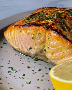 a piece of salmon on a plate with lemon wedges