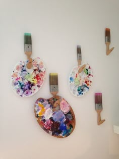 three paintbrushes are hanging on the wall next to two plates with flowers painted on them