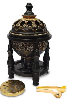 an ornate black and gold urn with two spoons next to it on a white background