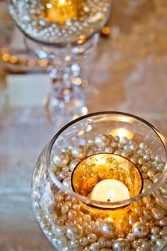 two wine glasses filled with pearls and a lit candle on top of a marble table