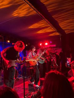 a band playing on stage at a concert with red lights and people watching from the sidelines