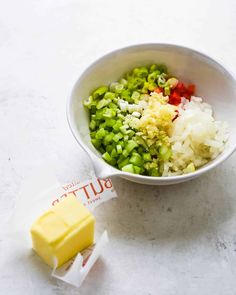 a white bowl filled with chopped vegetables next to a butter cube on top of a table