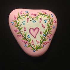 a pink painted rock with a heart and flowers on the top, sitting on a black surface