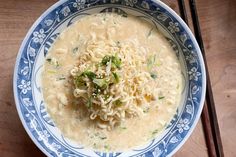 a blue and white bowl filled with noodle soup next to chopsticks on a wooden table