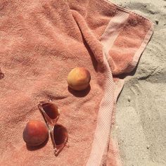 three peaches and two seashells on a towel at the beach with sand