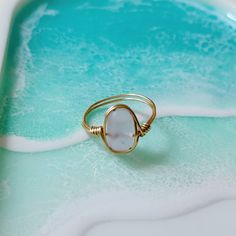 a gold ring with a white stone in the middle on a blue and green background