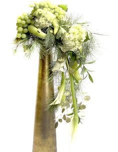 a tall metal vase filled with flowers and greenery