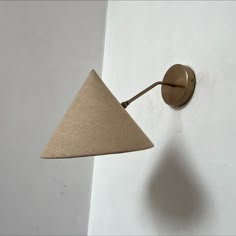 a wall light with a cone shaped shade on it's side and a white wall in the background