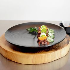 a black plate topped with sliced cucumbers and other food on top of a wooden platter