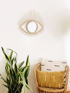 a wicker chair next to a potted plant and an eye shaped mirror on the wall