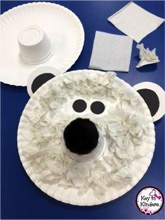 paper plate polar bear craft on a blue table with white plates and supplies for making it