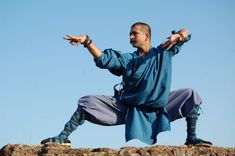 a man in blue is doing yoga on top of a rock wall with his arms stretched out