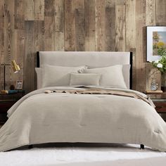 a bed in a room with wooden walls and white sheets on the headboard, along with two nightstands