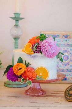 a white cake with oranges and pink flowers on it sitting on top of a table