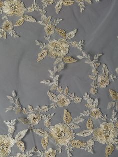 an embroidered fabric with flowers and leaves is shown in gold on grey background, closeup