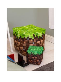 a green and brown cube shaped ottoman sitting on top of a floor next to a black object