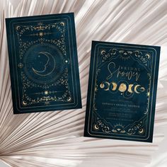 two blue and gold wedding cards with the moon on them, sitting next to each other