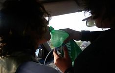 two people sitting in a car and one is holding a green bag