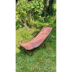 a red and white striped chaise lounger in the grass next to some trees