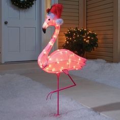 a lighted flamingo standing on top of snow covered ground next to a christmas wreath