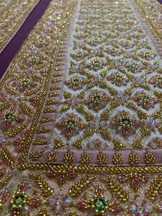 an intricately designed rug with gold and green beads on the bottom, in front of a purple background