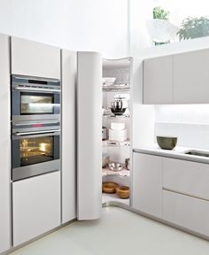 an open refrigerator in a white kitchen with lots of counter space and light coming from the door