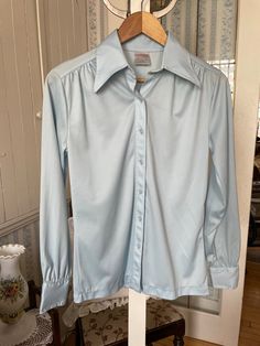 This pretty, super comfortable blouse is made of 100 per cent polyester that is stretchy, lightweight, silky and doesn't crease! It has the original buttons in the front and on the cuffs, a wide pointed collar and gathered yokes on the front and back. In very good vintage condition. Marked size 13, but vintage sizes are often much smaller than today's. The measurements, taken with the blouse lying flat, are: shoulder to shoulder, 16 inches; armpit to armpit, 19 1/2 inches; sleeves, 24 1/2 inches; overall length, 26 inches; bottom edge, 18 inches. Baby Blue Shirt, Comfortable Blouses, Vintage Sweaters, Blue Shirt, Vintage Baby, Denim Button Up, Baby Blue, Button Up Shirts, Vintage Ladies