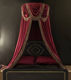 a bed with a red canopy over it and pillows on the bottom side, in front of a black wall