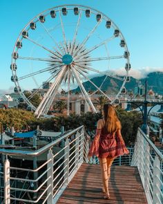 a woman walking across a wooden bridge next to a ferris wheel