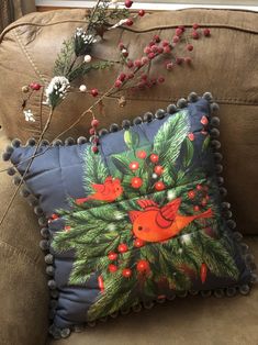 a christmas pillow on a couch with holly and red berries hanging from the back of it