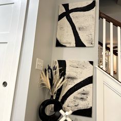 two paintings are hanging on the wall next to a black and white vase with feathers