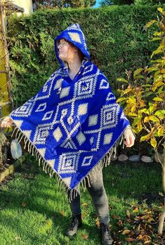 Our practical and comfortable poncho has a hood with strings for hood adjustment. It also features a button in the front, a big Kangaroo pocket and fringes at the end.  This warm yak wool blend poncho is made from yak wool  blended with viscose into yarns made in Himalayas. The yak wool itself is very harsh so has to be mixed with some other materials to become soft. They become beautiful pieces of tribal art made fashion. This blend maintains the thermo-balance characteristics of the product an Traditional Hooded Winter Poncho, Traditional Blue One-size Poncho, Traditional Blue Poncho, Blue Bohemian Cape Shawl, Hippie Hooded Poncho For Festivals, Traditional One Size Hooded Poncho, Bohemian Hooded Cape For Outdoor, Bohemian Handwoven Poncho For Winter, Bohemian Blue Cape Poncho