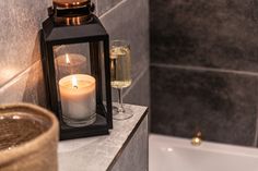 a candle is lit next to a bathtub with a glass of wine in it