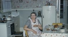 an older woman sitting at a kitchen table in front of a white refrigerator freezer