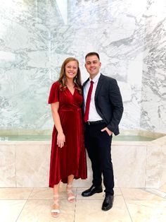 a man and woman standing next to each other in front of a marble wall with columns