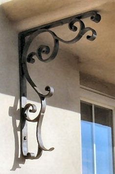 an iron bracket on the side of a building with a window in the back ground