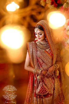 a woman in a red and gold bridal outfit standing with her hands on her hips