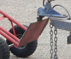 a red and blue hand truck with chains attached to it's front wheels on gravel ground