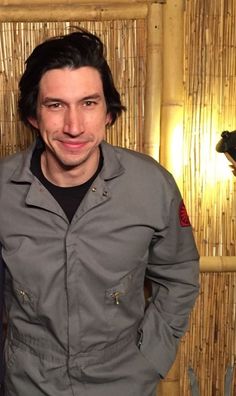 a man standing in front of a bamboo wall wearing a gray jacket and black shirt