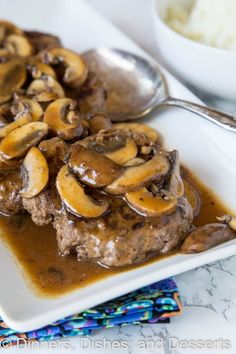 a white plate topped with meat and mushrooms covered in gravy