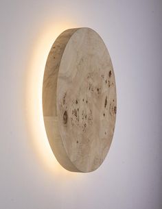 a wooden clock mounted to the side of a white wall with a light on it