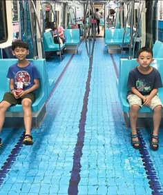 two young boys sitting on blue seats in a public transportation car with tile flooring